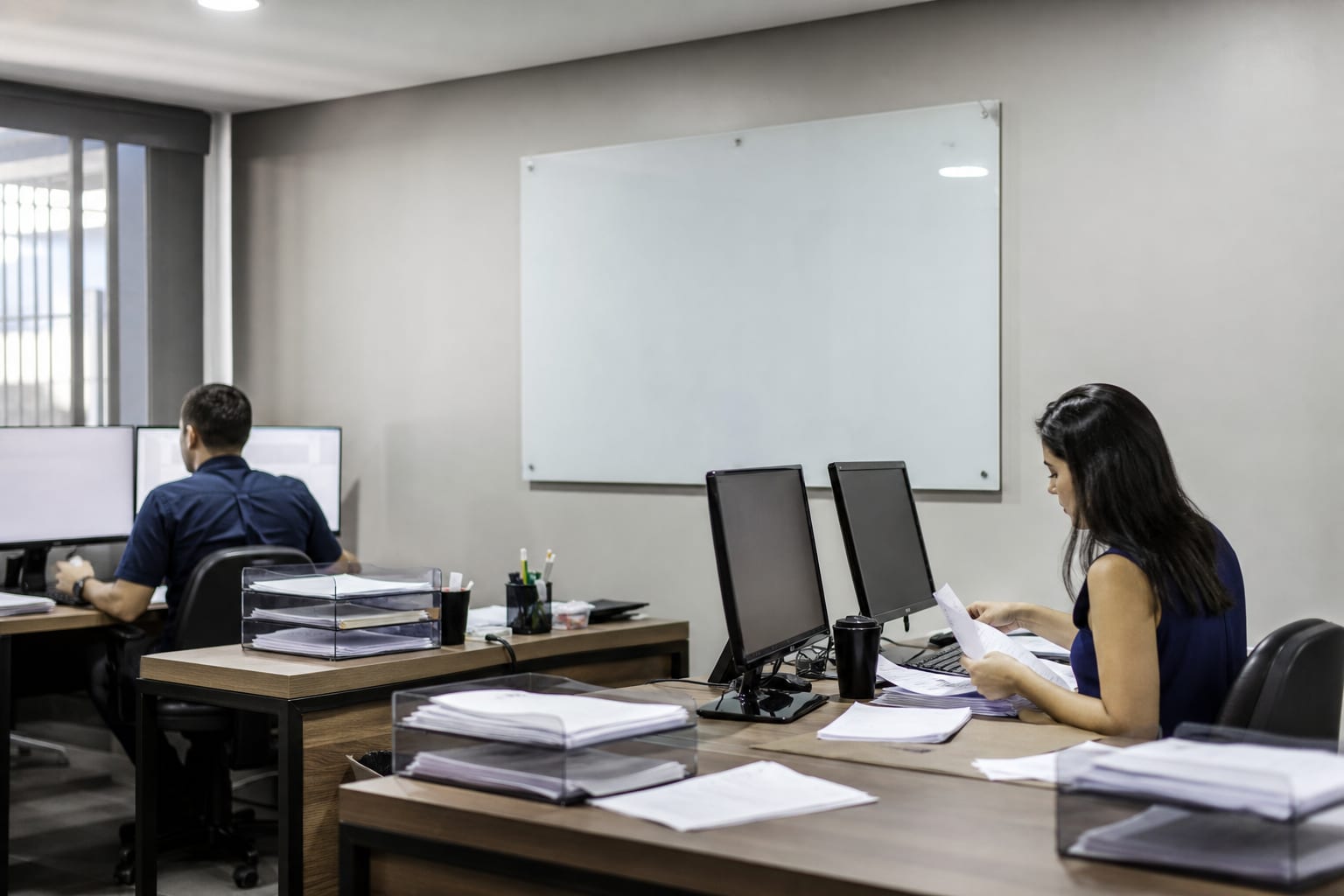 Dupla trabalhando na sala de departamento pessoal de um escritório contábil com monitores e bandejas de papel